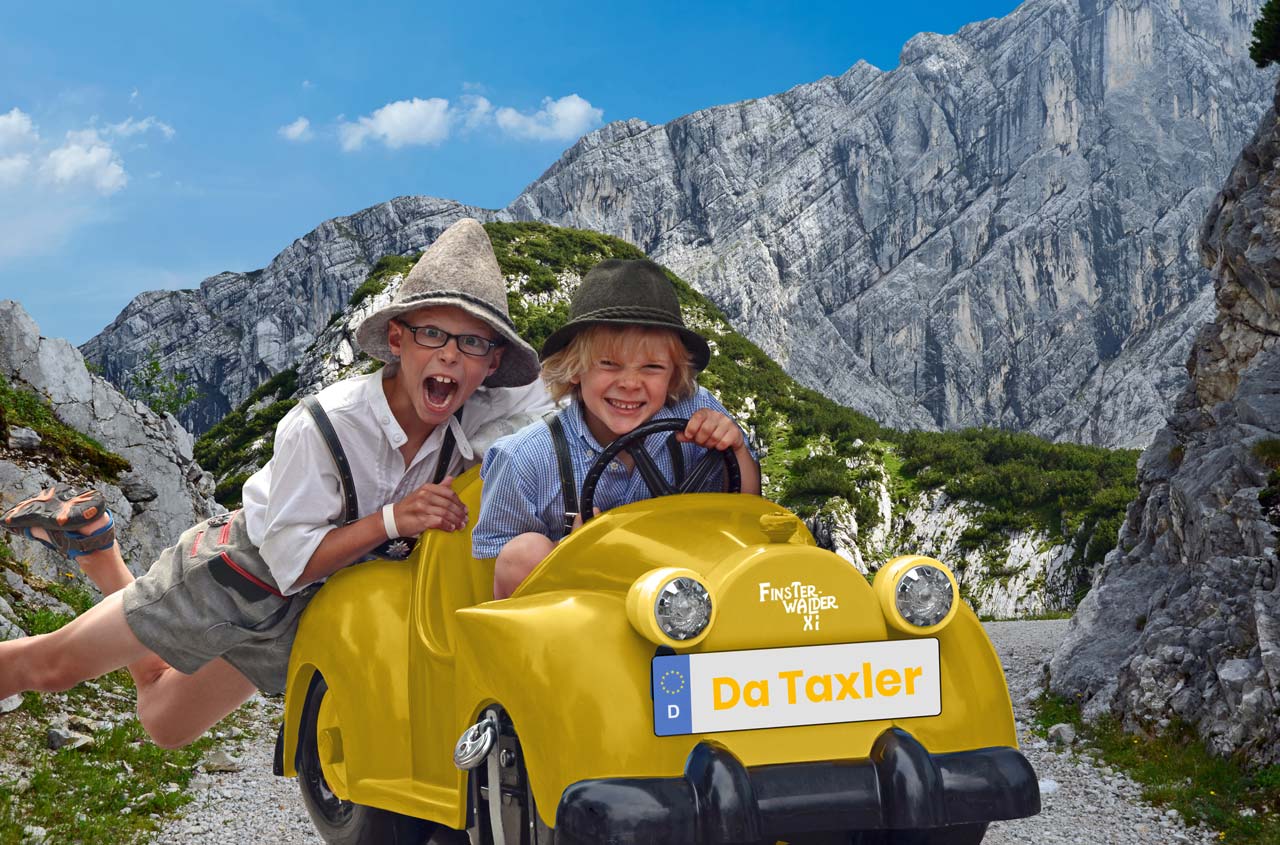 Ein lustiges Bild mit 2 Kindern. Ein Kind sitzt in einem Spielzeug Taxi und grinst. Das zweite kind hängt hinten dran mit den Füßen in der Luft und schreit.